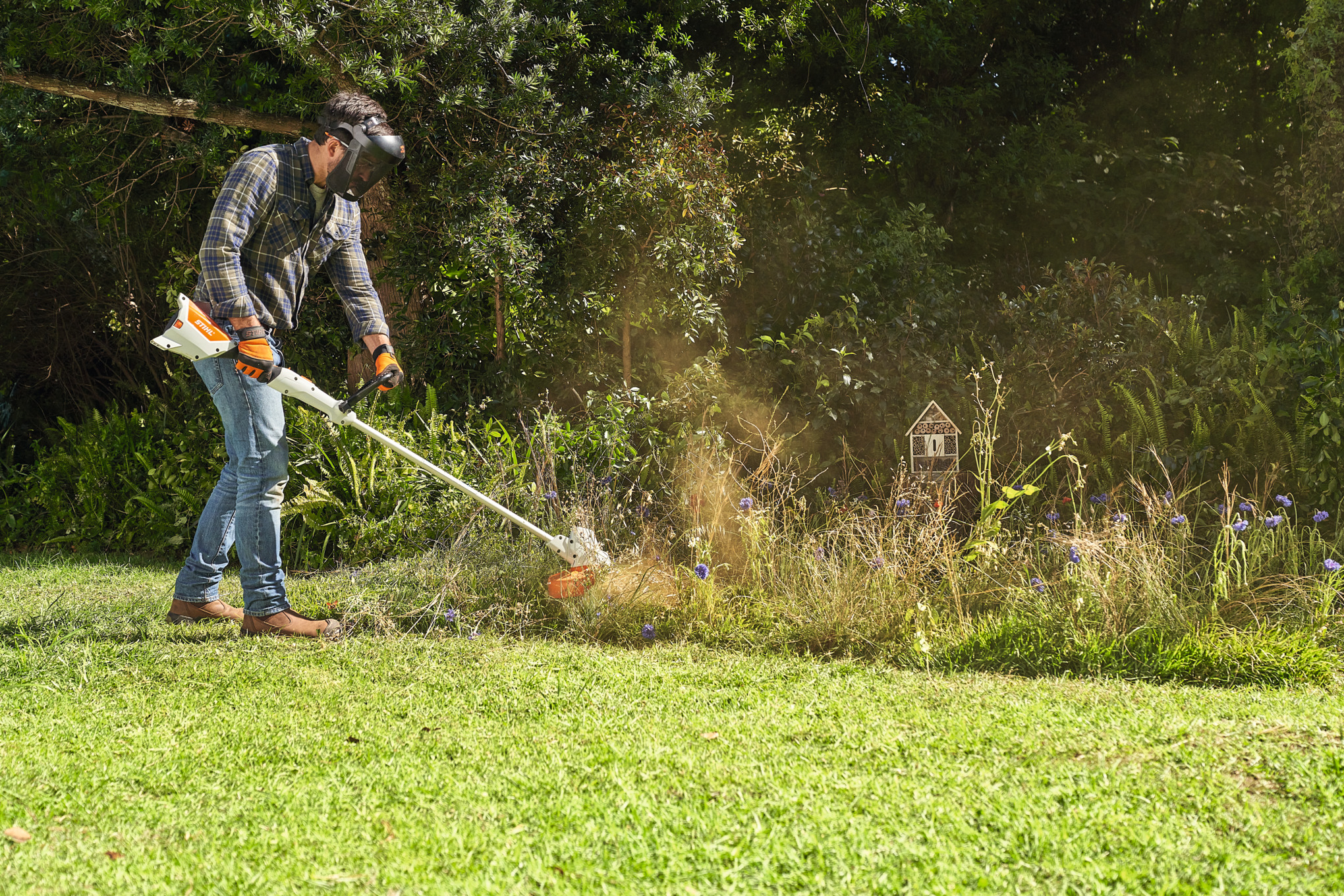 STIHL FSA 57で野性の花畑を刈っている男性