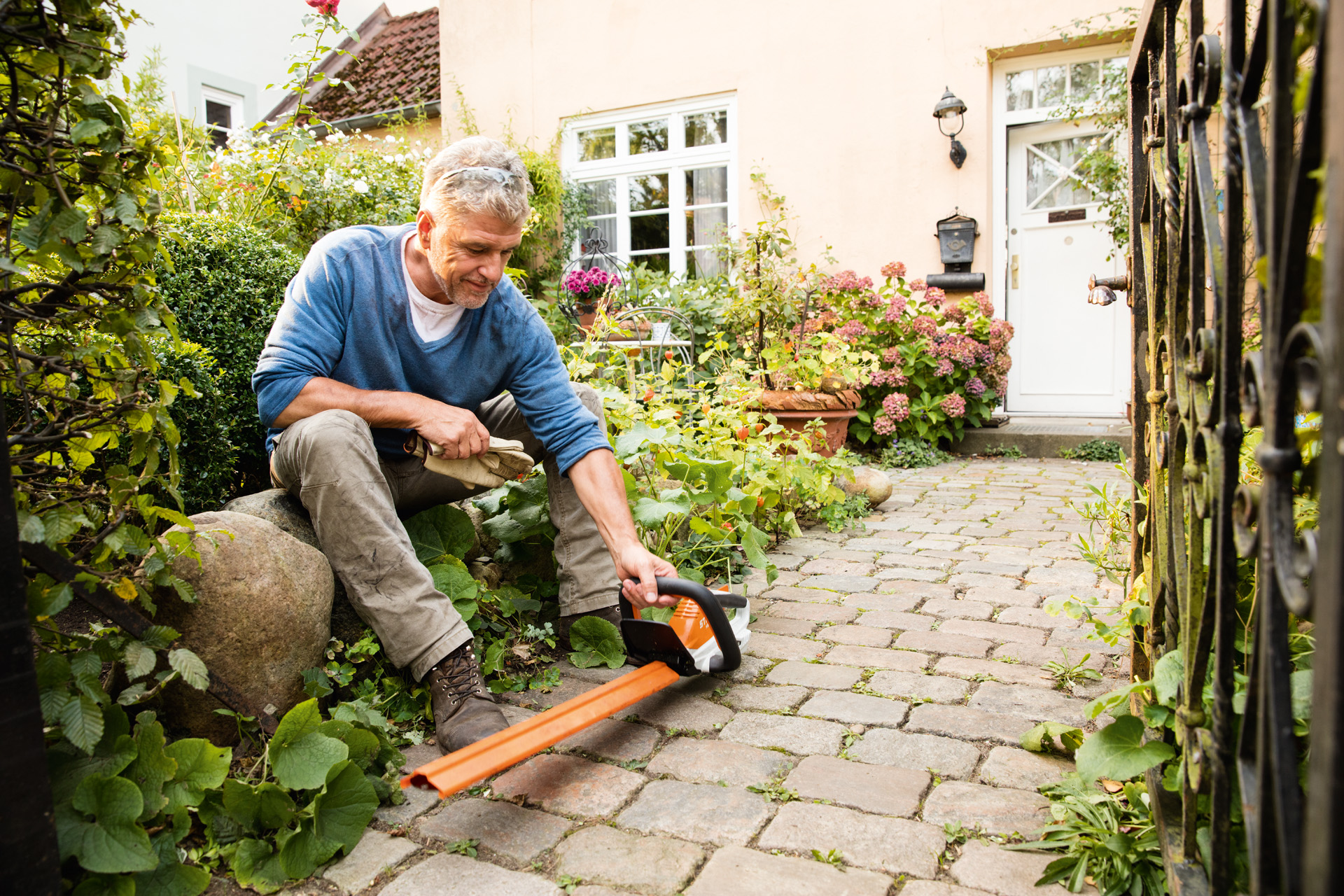 STIHL AIラインの電動ヘッジトリマーHSA 45を持って家の前に立つ男性