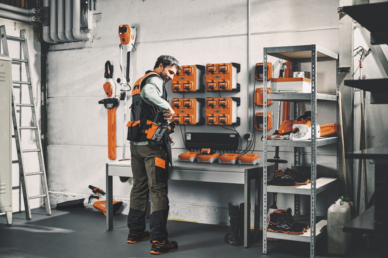 STIHLツールとバッテリーを保管する倉庫でモジュール式ハーネスシステムSTIHL ADVANCE X-Flexを装着する男性 