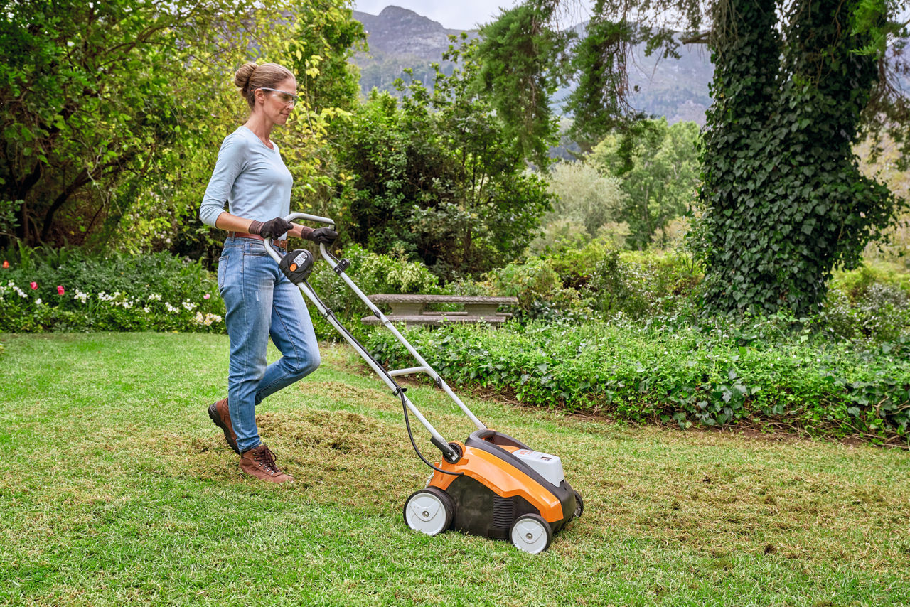 安全メガネと保護手袋を着用した女性が STIHL 芝刈り機で牧草地を刈る